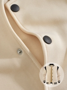 Detail of cream fleece varsity jacket featuring black matte metal snap button closure