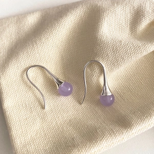Detail of minimalist lavender purple bead earrings on textured beige linen bag