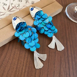 Detail of fish-shaped hair clips with blue shell scales and evil eye accents on wood