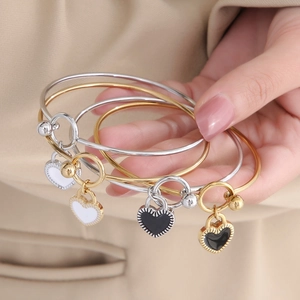 Macro shot of stacking gold and silver heart bracelets with black and white enamel charms
