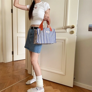 Detail of blue striped canvas tote with orange handles held by a model in a minimalist room