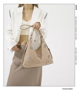 Detail of beige shoulder bag featuring silver butterfly charms and sleek nylon fabric