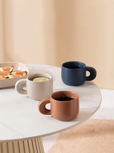 Three matte ceramic coffee mugs in beige, caramel and navy with large circular handles