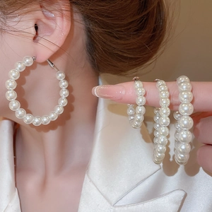 Detailed view of white pearl hoop earrings in multiple sizes on hand and ear