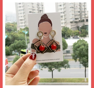 Détail de boucles d'oreilles géométriques dorées avec perles rouges sur carte