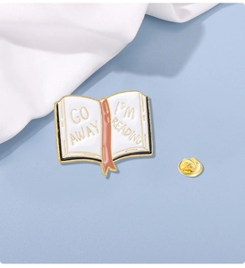 Detail of enamel book brooch with 'GO AWAY I'M READING' text and golden metal backing