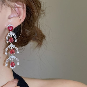 Detailed view of red heart and pear cut drop earrings with tiered tassels on model
