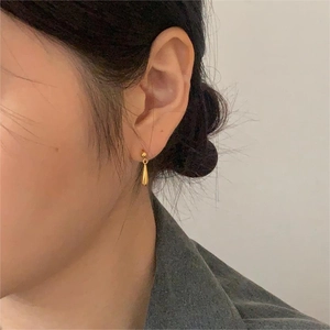 Dettaglio di un orecchino a goccia dorato minimalista indossato da una modella elegante