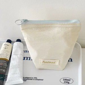 Creamy beige trapezoid makeup bag with light blue zipper and Purdored woven label