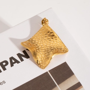 Vue macro d'un pendentif irrégulier en acier doré avec texture martelée sur un livre