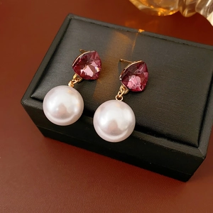Détail de boucles d'oreilles perles avec pierre violette et métal doré sur boîte