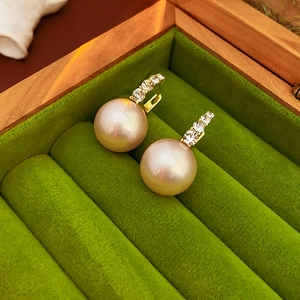Macro shot of pearl earrings with rhinestones and gold hooks in a green velvet box