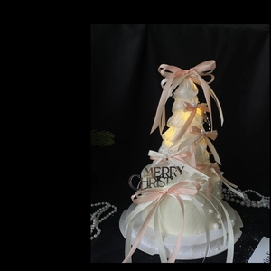 Close-up of white Christmas tree cake topper with pink bows, pearls and warm lights