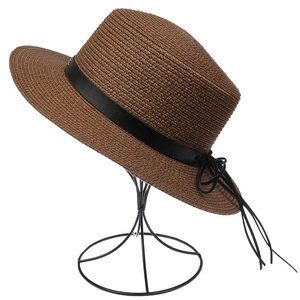 Detail of a brown woven straw sun hat featuring a black leather band and side bow knot