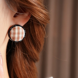 Close-up of a model wearing brown plaid fabric button earrings with a black border