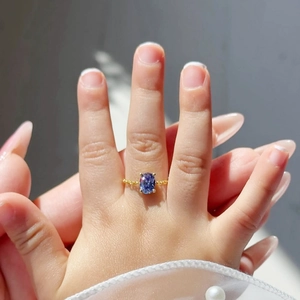 Detail of a gold-plated ring featuring an oval purple zircon and beaded band on a finger