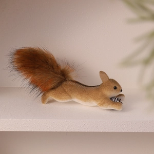 Realistic foam squirrel ornament with fluffy tail and pinecone on a white shelf