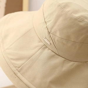 Close-up of beige sun hat fabric texture and metallic brand plaque detail