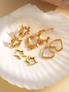 Detailed close-up of 18k gold earrings set with heart and star patterns in a seashell