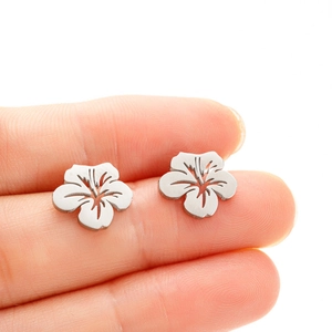 Close-up of minimalist stainless steel hibiscus flower stud earrings on finger showing size