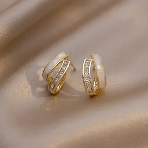 Macro detail of C-shaped gold-plated earrings with opal inlay and zircon stones