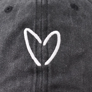 Close-up of white heart embroidery on a washed vintage black cotton baseball cap
