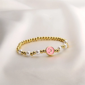 Détail d'un bracelet doré avec perles et pendentif lettre C en émail rose sur satin