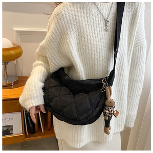 Detail of black quilted crossbody dumpling bag with a cute rabbit charm and wide strap