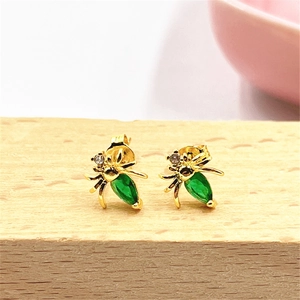 Macro shot of gold spider stud earrings with green gemstones on a wooden base