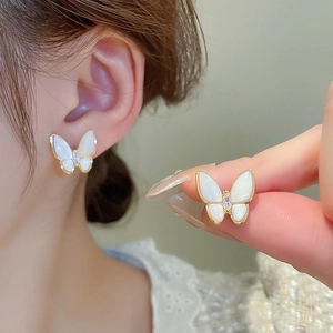 Détail de boucles d'oreilles papillon dorées avec ailes en nacre et zircon central