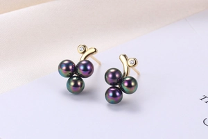 Macro shot of grape-shaped earrings with purple pearls and zircon studs on white silk