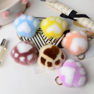 Variety of colorful rex rabbit fur cat paw keychains displayed with lifestyle props