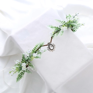 Macro detail of fairy flower crown with green leaves, white flowers and silver pendant