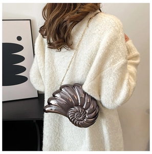 Detail of seashell shaped metallic crossbody bag with gold chain on model in white sweater