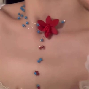 Nahaufnahme einer blauen Perlenkette mit roter 3D-Blume am Hals eines Models