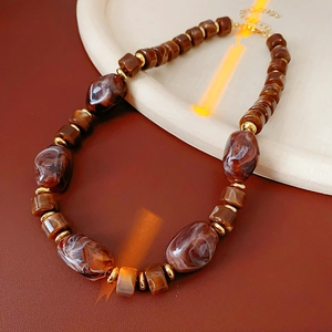 Dettaglio di perle marmorizzate marroni e accenti in metallo dorato sulla collana