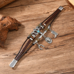 Detail of brown leather bracelet with turquoise cross and cowboy-themed lucky metal charms