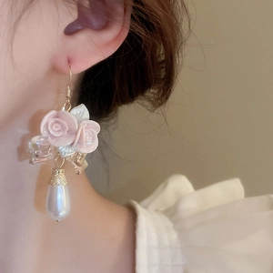 Close-up of pink ceramic roses and white teardrop pearl earrings worn by a model