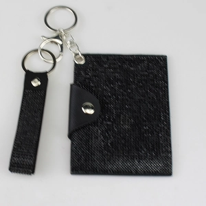 Black woven texture card holder with metal snap button and keychain attachment on grey background