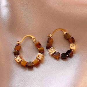 Détail de boucles d'oreilles créoles dorées avec perles cubes léopard sur de la soie