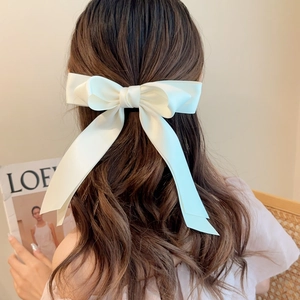 Elegant white satin bow hair clip with long ribbons styled on long wavy brown hair