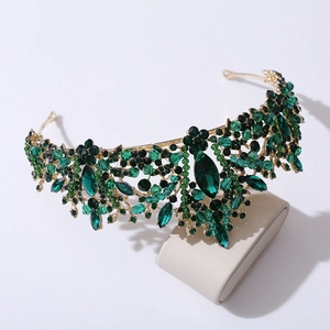 Elegant gold bridal crown featuring green leaf crystals and rhinestones on a beige stand