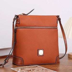 Close-up of brown pebbled leather texture on crossbody bag over warm wooden background