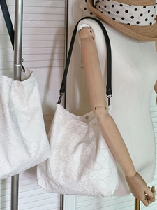 Detail of white cotton tote bags with 3D leaf embroidery and black leather straps