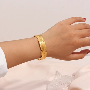 Close-up of golden feather open cuff bracelet showing detailed leaf texture on wrist