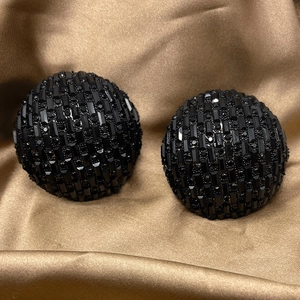 Close-up of hemispherical stud earrings featuring black pave-set crystals on gold silk fabric