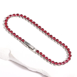 Detailed close-up of a silver tennis bracelet with red zircons on a white stone background