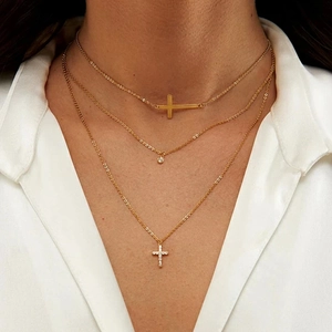 Close-up of a three-layer gold necklace with cross and crystal pendants on a model