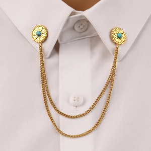 Close-up of golden collar pins with turquoise stones and double chains on a white shirt
