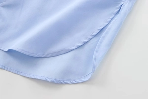 Détail de l'ourlet incurvé et de la fente latérale d'une chemise en coton bleu clair pour femme